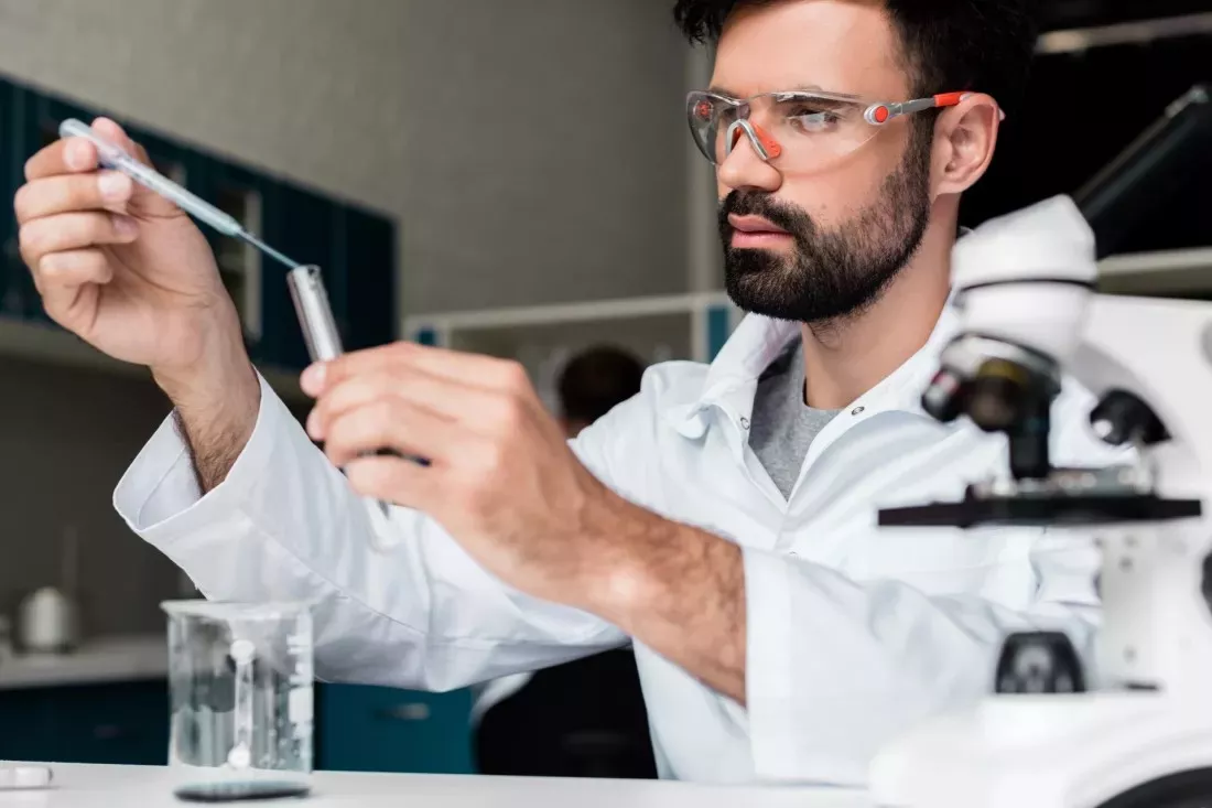 Cientifico con gafas de proteccion mide con una pipeta una muestra en un tubo de ensayo en un laboratorio de quimica