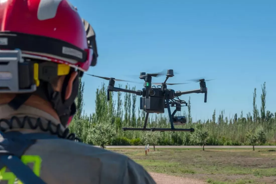 Bombero con casco observa un dron que vuela sobre un campo